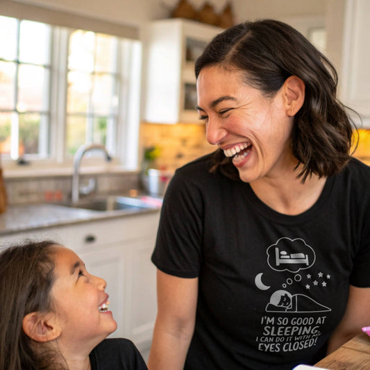 Mother and child laughing, mom in a black "I'm so good at sleeping" t-shirt, celebrating joyful mom life and humor.