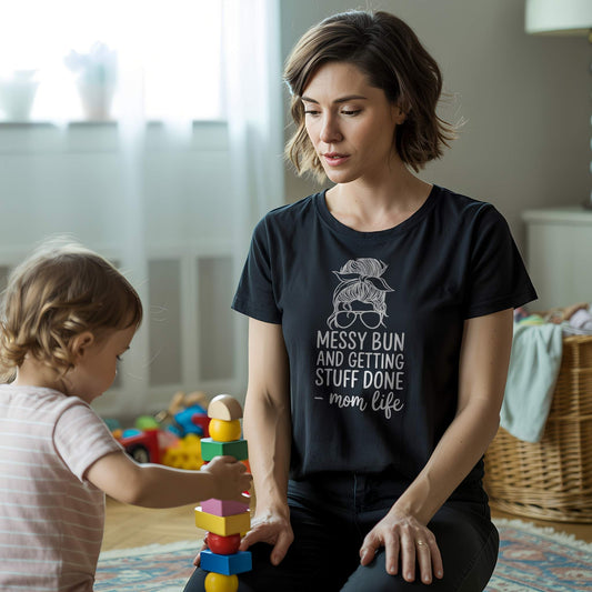 Mom in Black "Messy Bun" t-shirt playing with child, showcasing everyday mom life and parent humor.