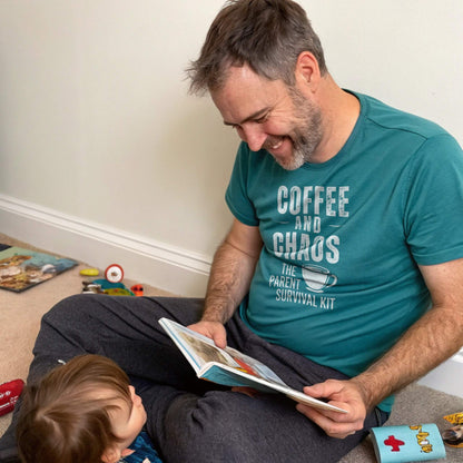 A dad in a Heather Deep Teal "Coffee and Chaos" t-shirt, laughing while reading to a child, showing relatable parenting humor and connection.