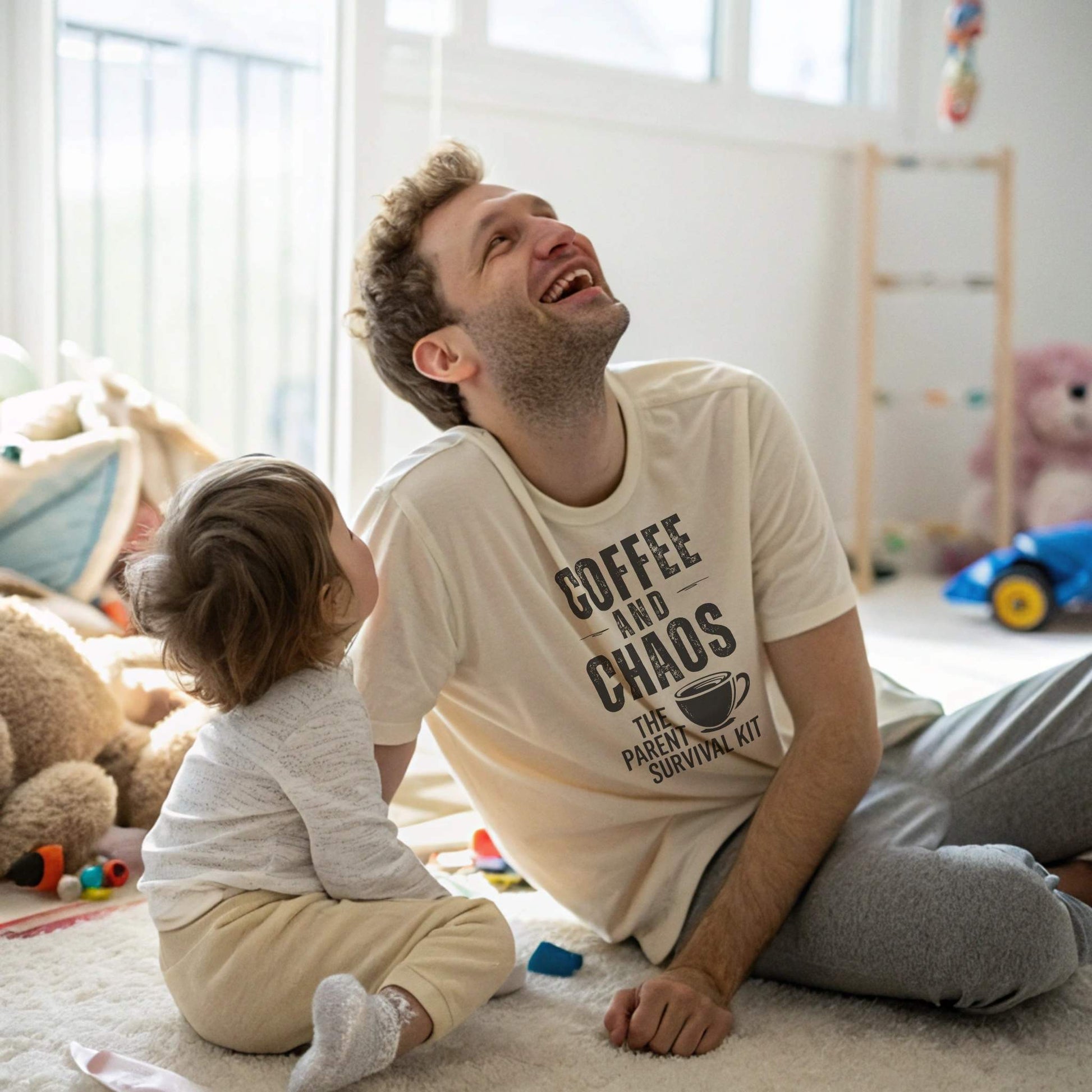 A dad in a Soft Cream "Coffee and Chaos" t-shirt, laughing with a toddler, illustrating the joy and humor amidst parenting chaos.