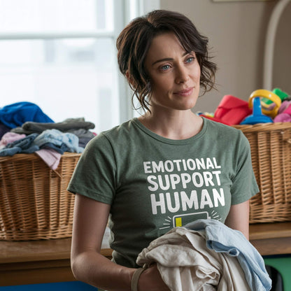 Lifestyle Photo - Mom; Female parent wearing a Heather Forest "Emotional Support Human" t-shirt, folding laundry, representing the humorous chaos of mom life.