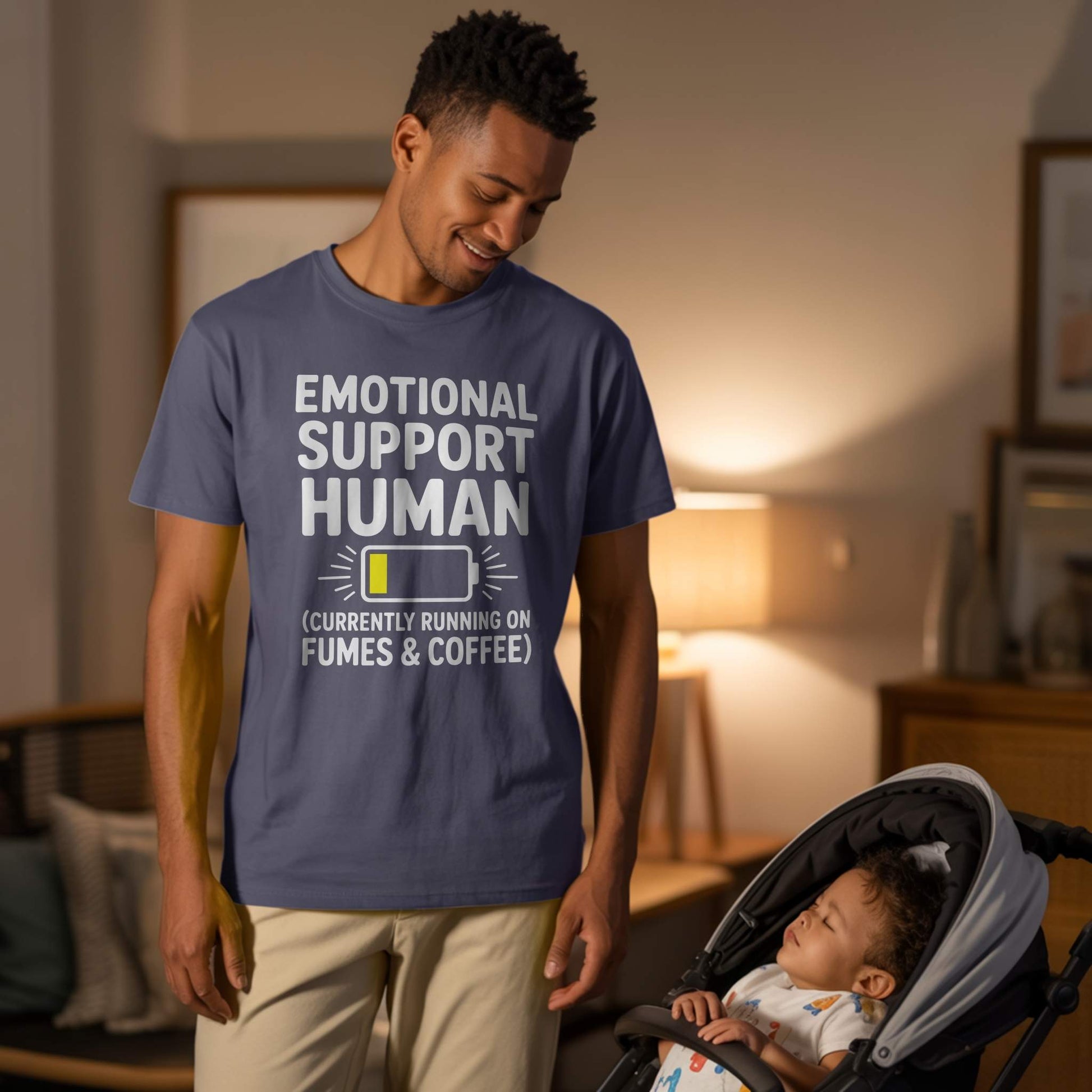 Lifestyle Photo - Dad & Baby; Male parent wearing a navy "Emotional Support Human" t-shirt, looking at a sleeping baby in a stroller, depicting caring dad life.