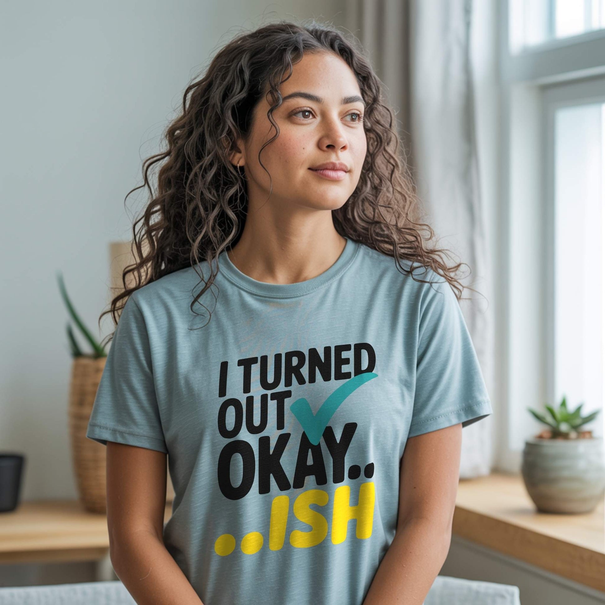 Woman wearing a Heather Prism Dusty Blue t-shirt with the "I Turned Out Okay...ish" graphic, offering comfort and understanding.