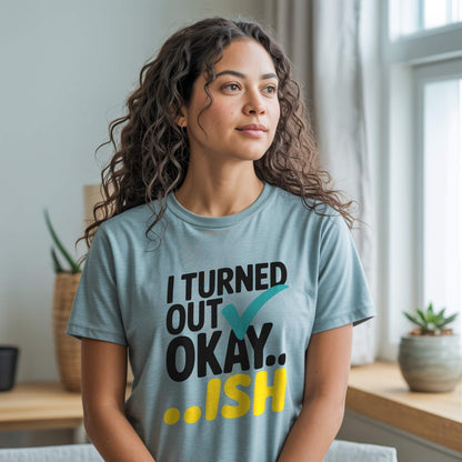 Woman wearing a Heather Prism Dusty Blue t-shirt with the "I Turned Out Okay...ish" graphic, offering comfort and understanding.