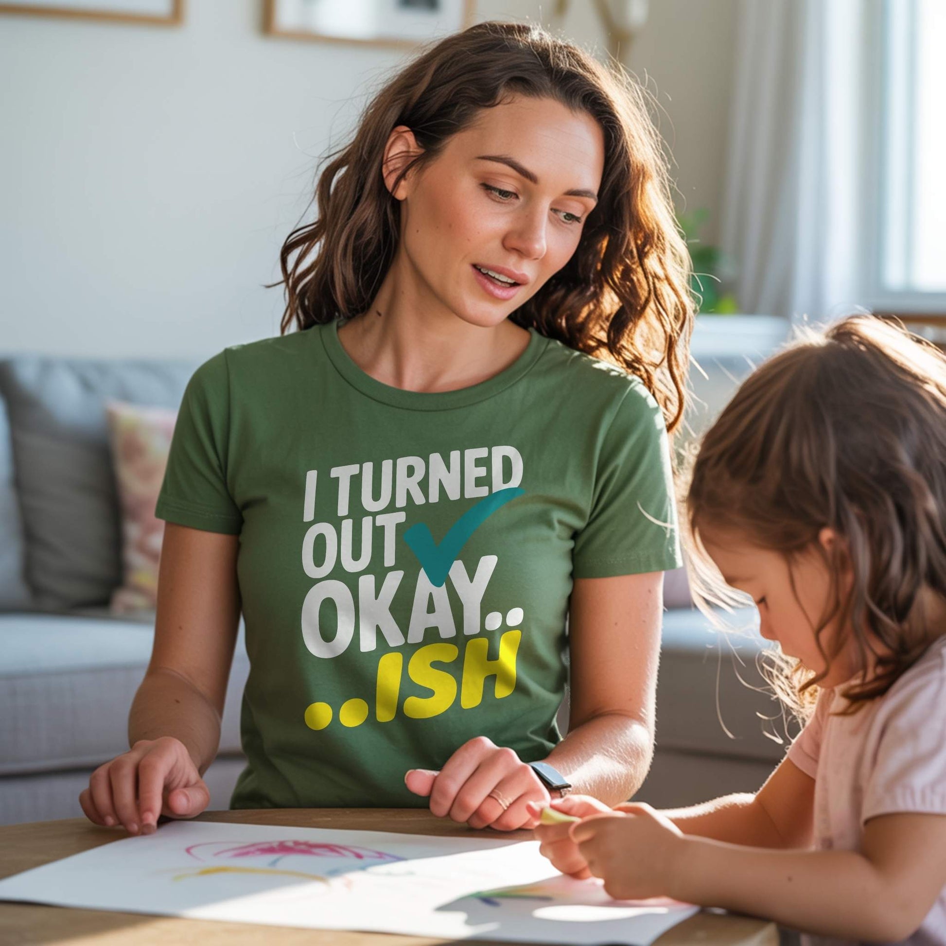 Mom in a Forest green "I Turned Out Okay...ish" t-shirt, smiling while coloring with her child, reflecting real parent life.