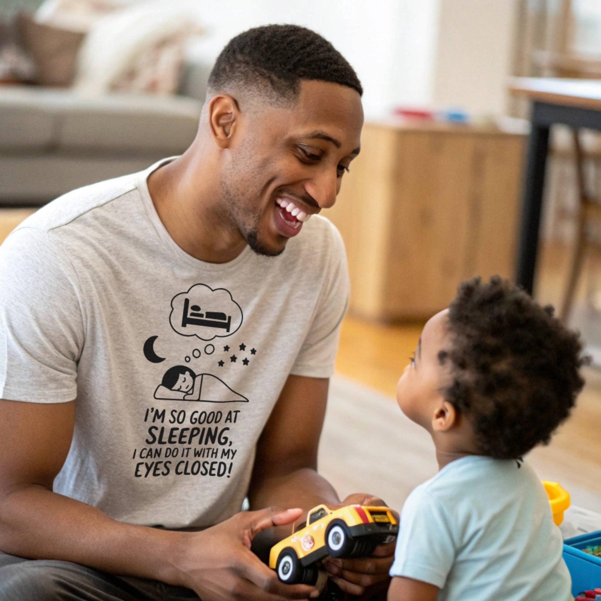 Father and child playing, dad in a heather dust "I'm so good at sleeping" t-shirt, embracing dad life and playful moments.