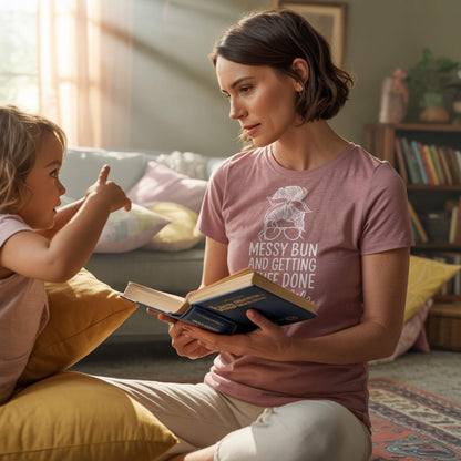 Relatable mom in Heather Mauve "Messy Bun" t-shirt reading with child, a cozy parenting moment.